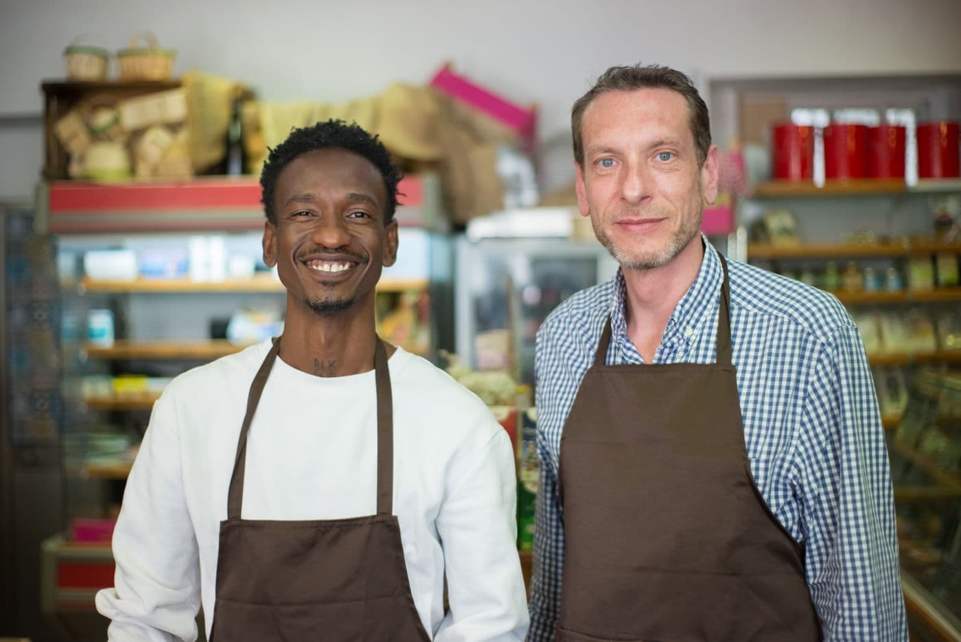 Dois sócios de avental, sorrindo dentro da mercearia